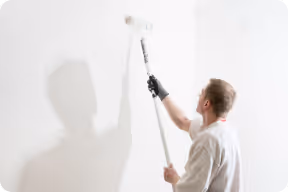 Mann streicht mit Farbroller eine weiße Wand.