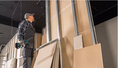 Handwerker installiert Trockenbauwände mit Schraubendreher auf Baustelle.